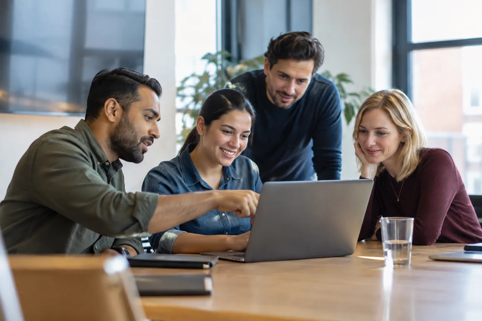 A realistic photograph of a small group of colleagues looking at a laptop together in an office setting.